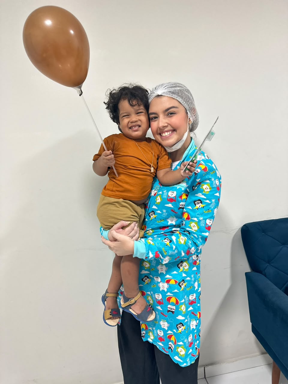 Dra. Thirza Nunes sorrindo com uma criança acolhida no colo após o atendimento odontopediátrico